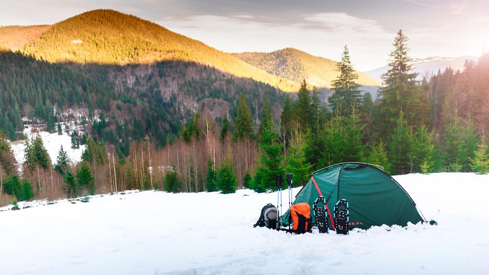 Tent. backpacks. trekking poles, snowshoes on snow in the mountains