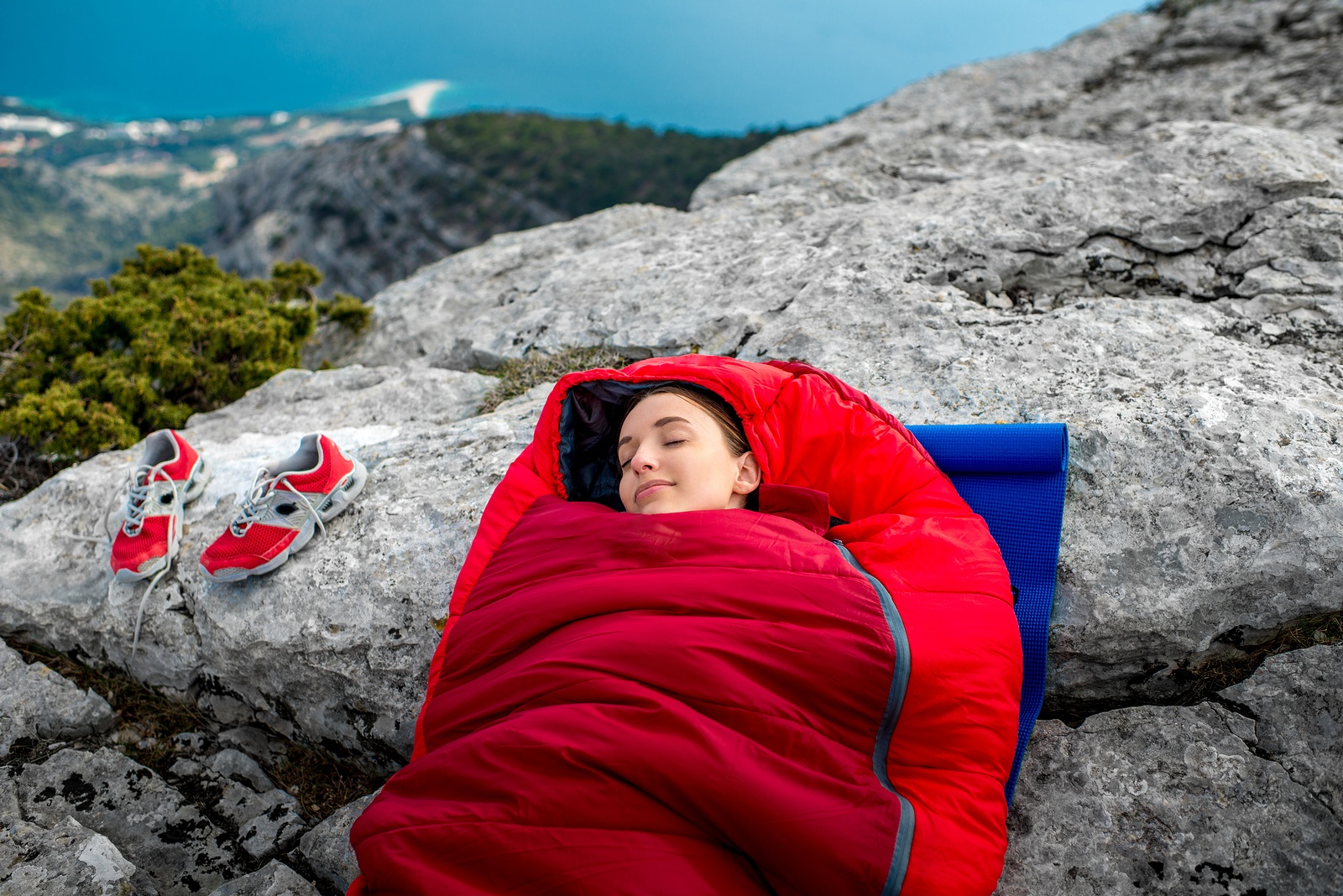 Young woman sleeping in red sleeping bag on the rocky mountain