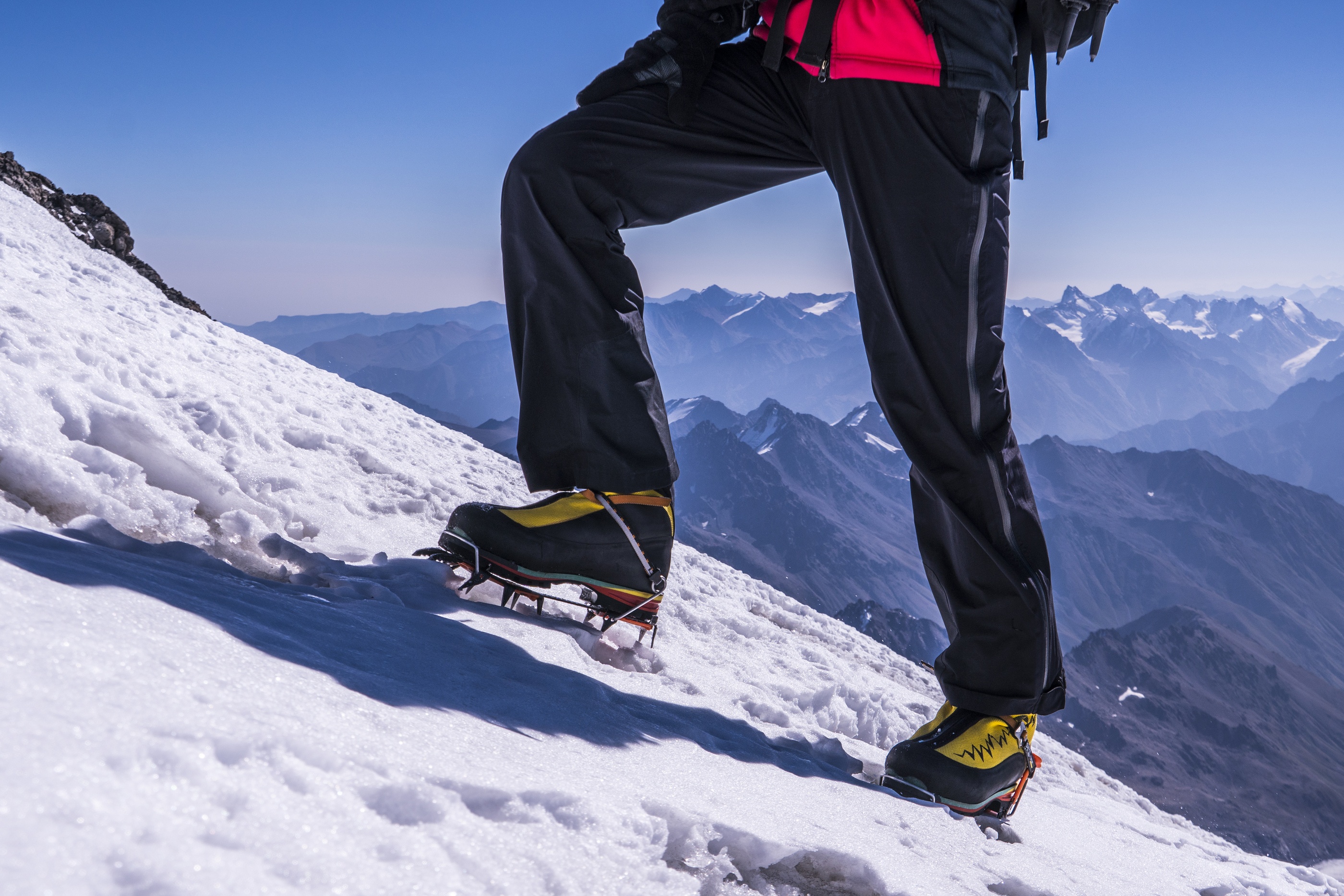 an legs in crampons come to the top of mountain. Feet in trekking boots on the background of the snowy Caucasus